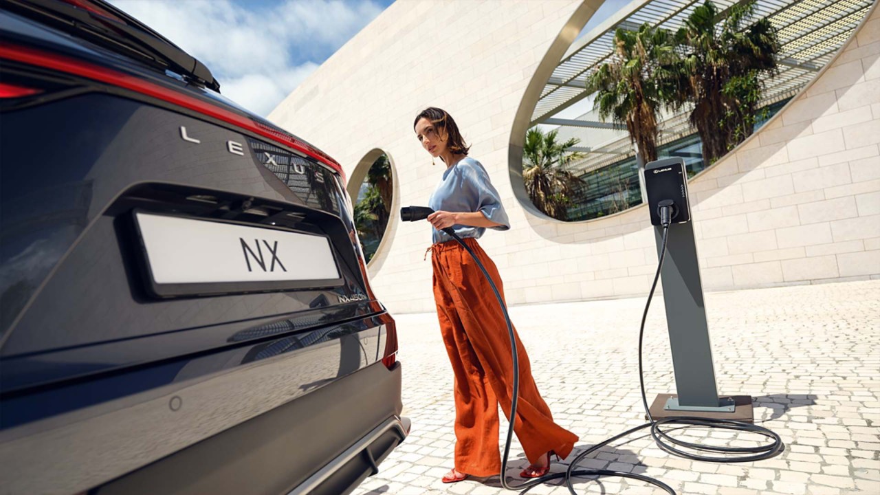 A person approaching a parked Lexus NX with a charger